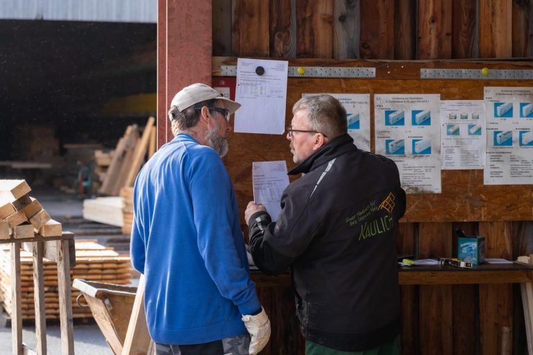 Ein Bild auf dem Gelände des Sägewerks der Firma Kaulich, wo zwei Mitarbeiter im Gespräch zu sehen sind.